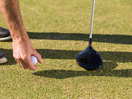 Man's hand placing a golf ball on a tee.