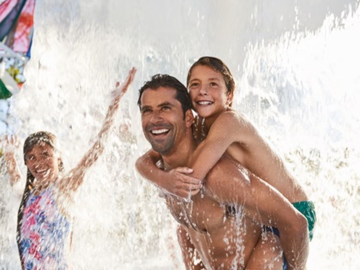 Dad giving son a piggyback with water splashing around them.
