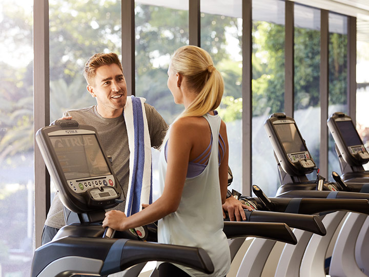 Two people smiling together by the treadmills at RACV Royal Pines' One Lifestyle fitness centre.