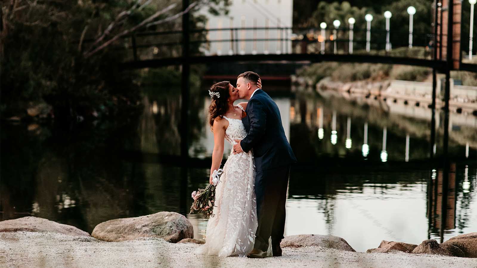 Bride and groom kissing at the Royal Pines resort, in front of a serene pond.