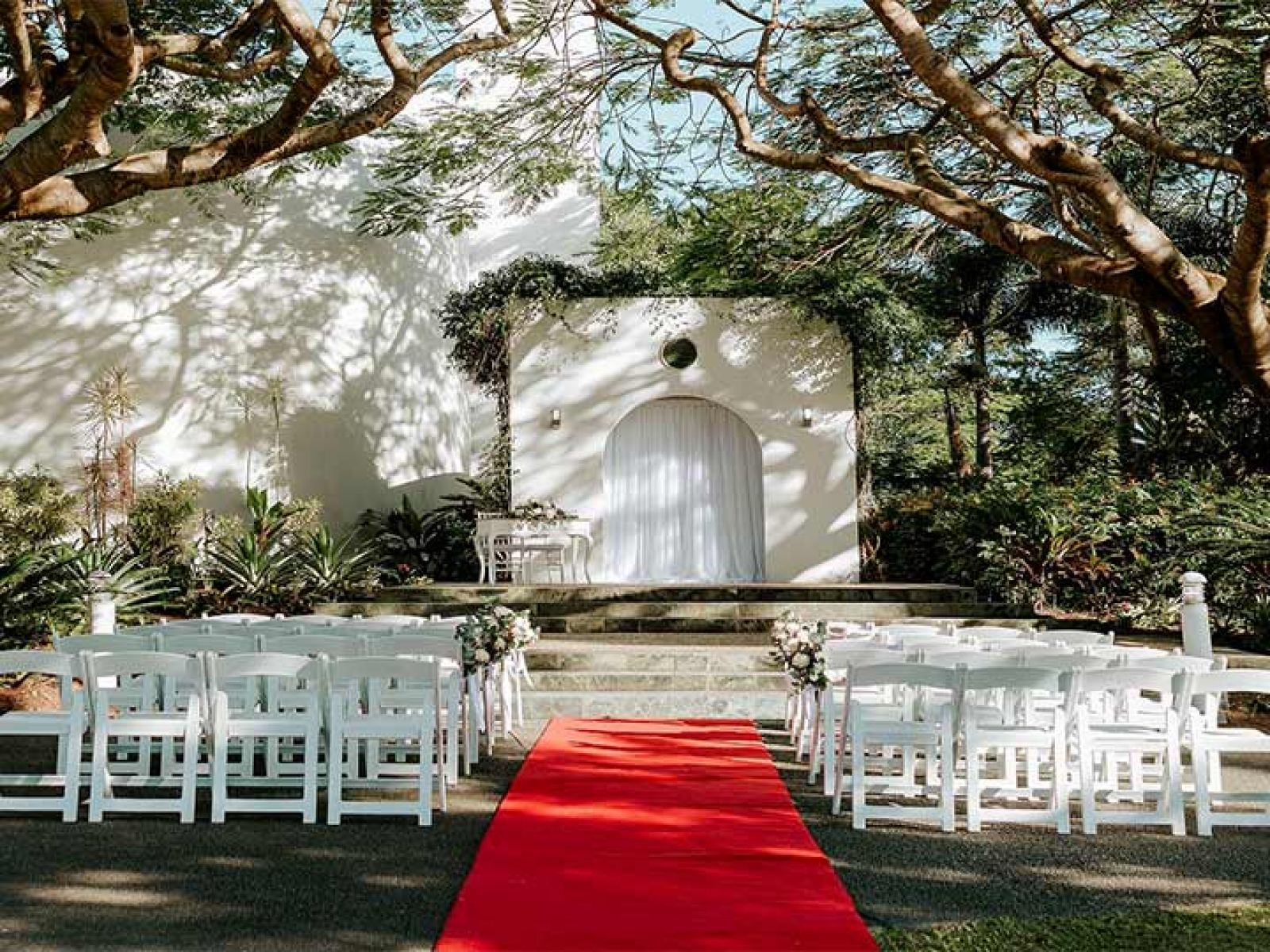 Outdoor wedding ceremony at the Royal Pines garden steps, featuring Poinciana trees and a red carpet. 