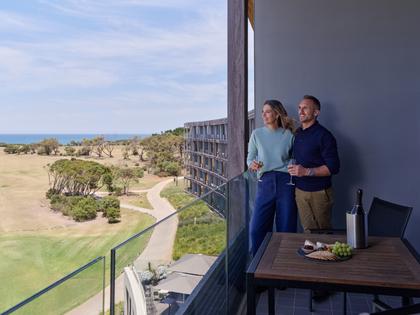 Couple standing on the balcony enjoying a view with a glass of wine and nibbles. 