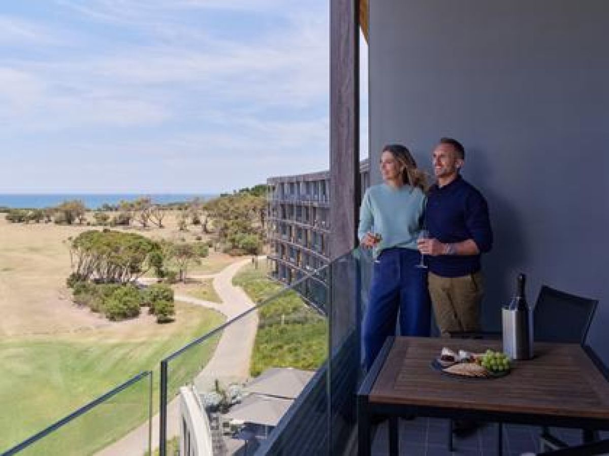 Couple standing on the balcony enjoying a view with a glass of wine and nibbles. 