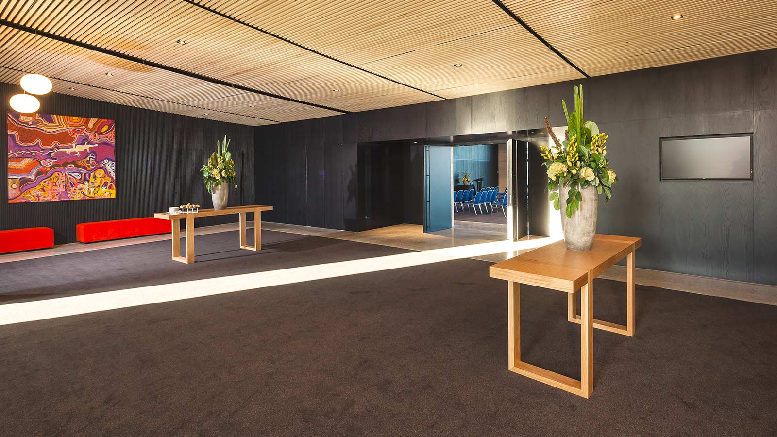 Great Ocean Road Ballroom's pre-function area at RACV Torquay Resort, featuring red benches and potted plants.