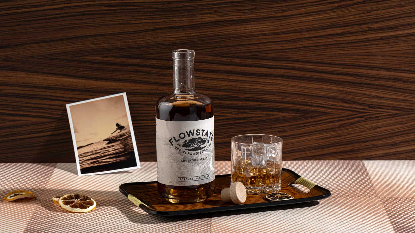 A bottle and glass of whiskey presented on a serving plate with dried fruit. 