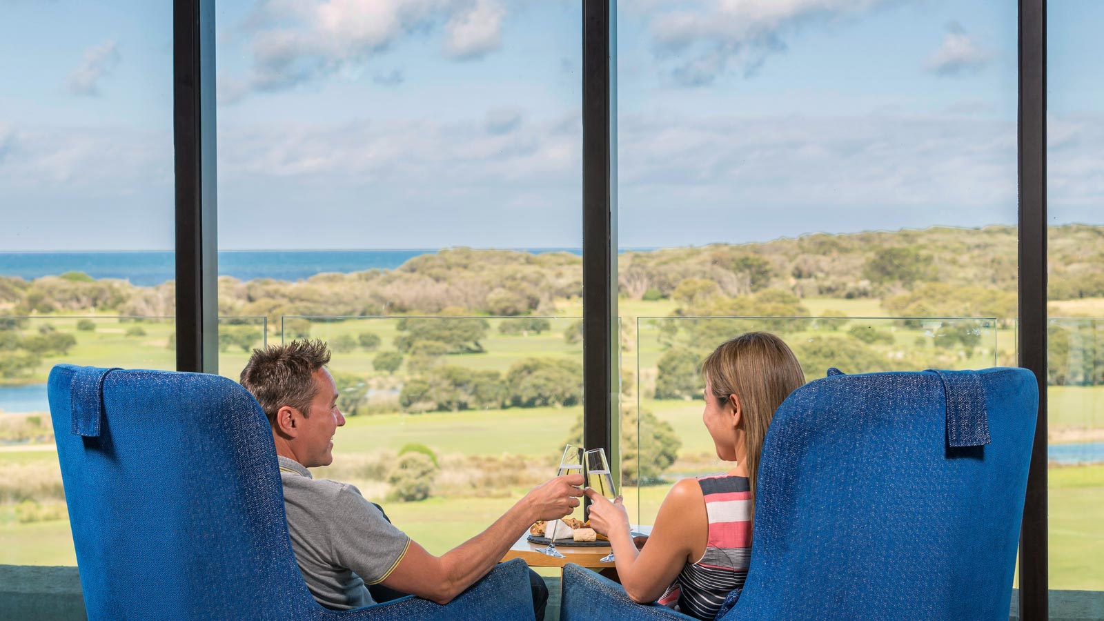 Couple sitting by floor to ceiling window having wine in Hardings Lounge at RACV Torquay Resort.