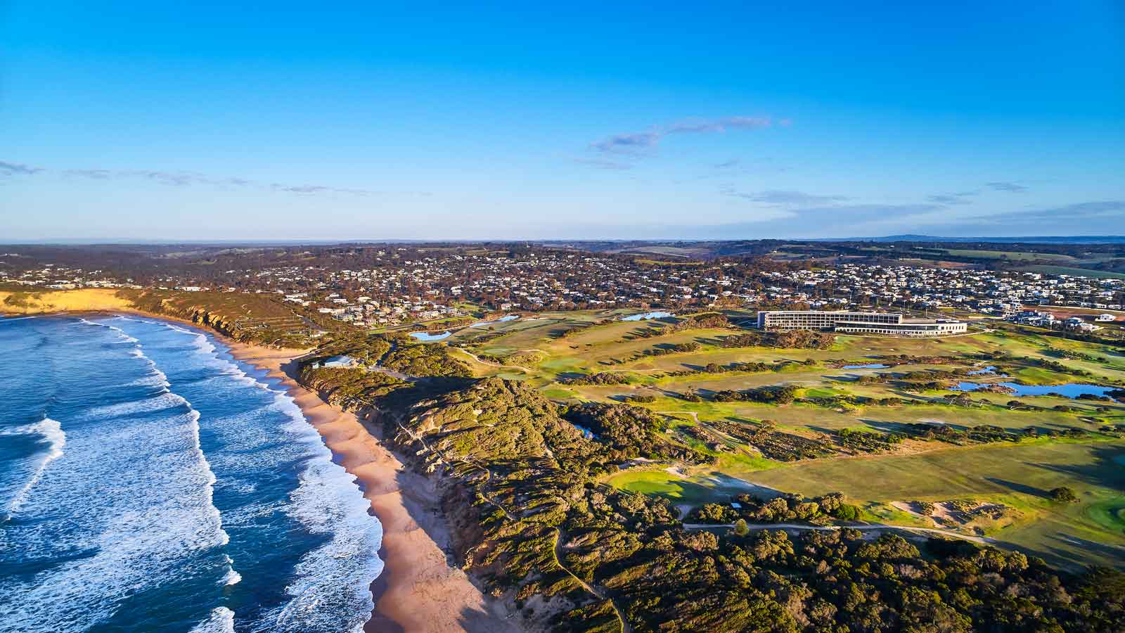 Aerial view of RACV Torquay resort with lush green grasses and the edge of the ocean.