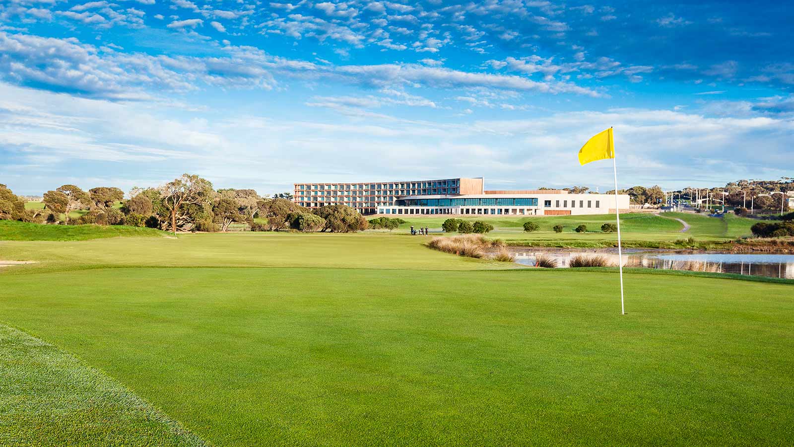 Yellow flagpole on the RACV Torquay golf course, in front of greenery and the resort.