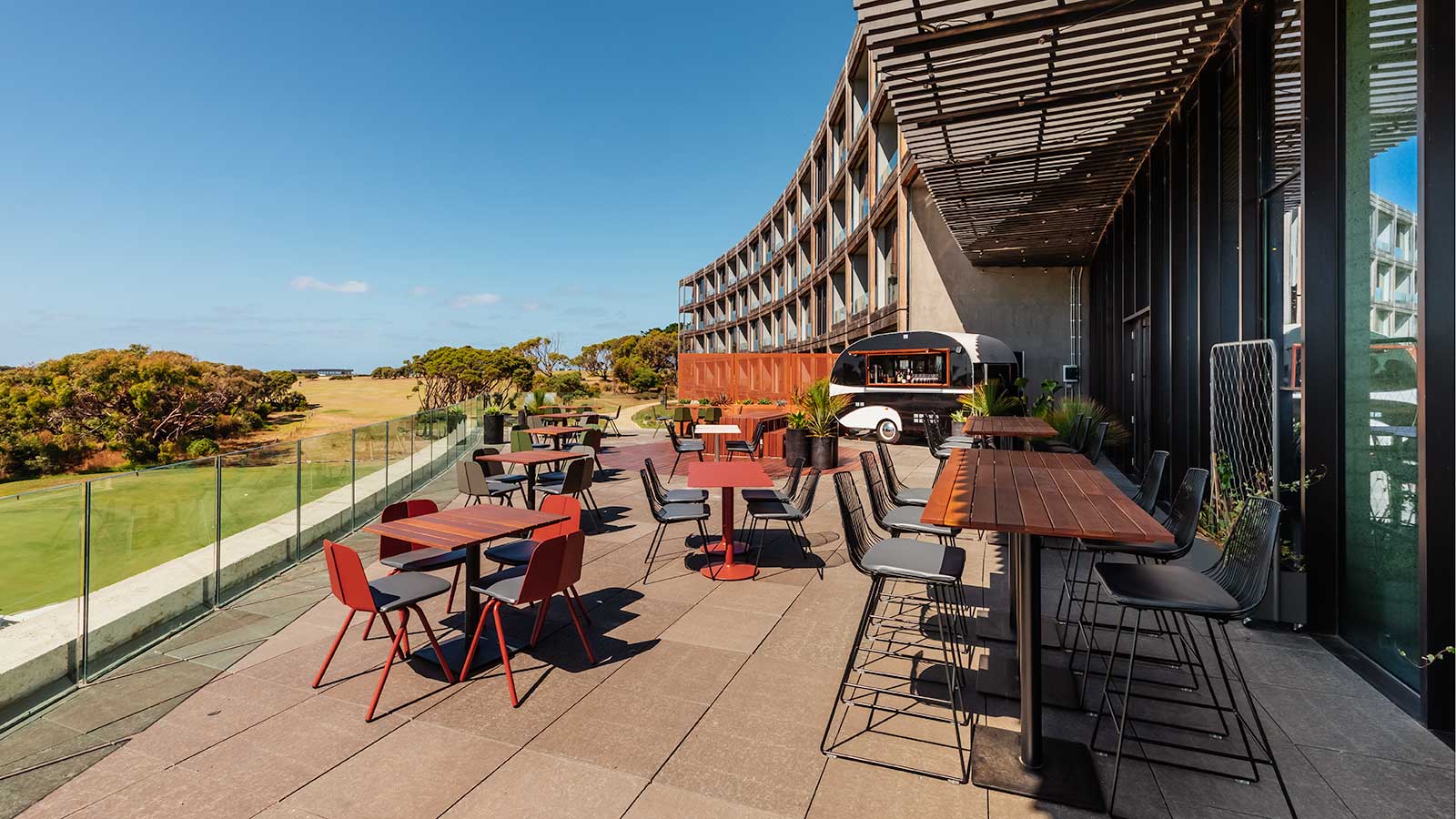 Outdoor terrace at RACV Torquay Resort, featuring tables and chairs and a parked drinks trailer.