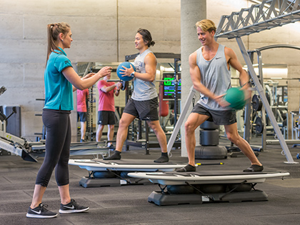 Personal trainer guiding two people through an exercise using medicine balls and balance boards, at RACV Torquay Resort's One Lifestyle fitness centre.