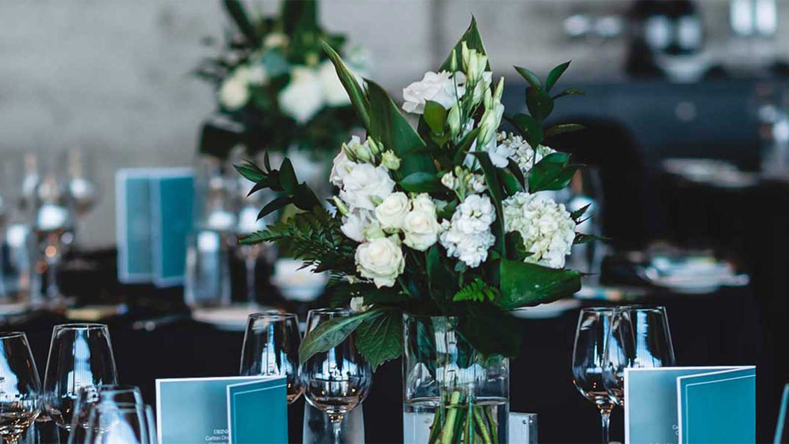 Table setting including menus, glassware and a flower centrepiece.