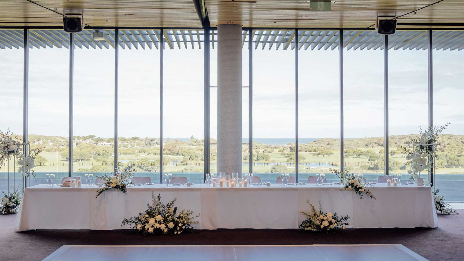 A long table infront of tall windows decorated with flowers and candles for the wedding party.