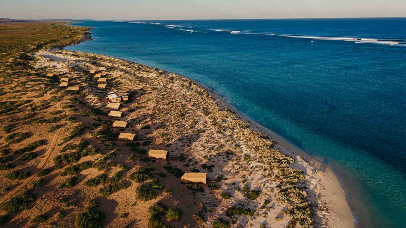 Several beach huts nestled along the rugged coast with blue waters. 