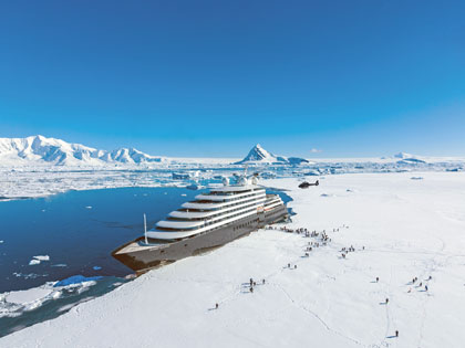 An icebreaker cruise ship docked on the edge of ice in Antarctica with people disembarking. 