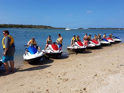 People sitting on jetskis along the shore of a beach.