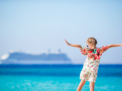 Young girl posing in front of a cruise ship sailing on the horizon.
