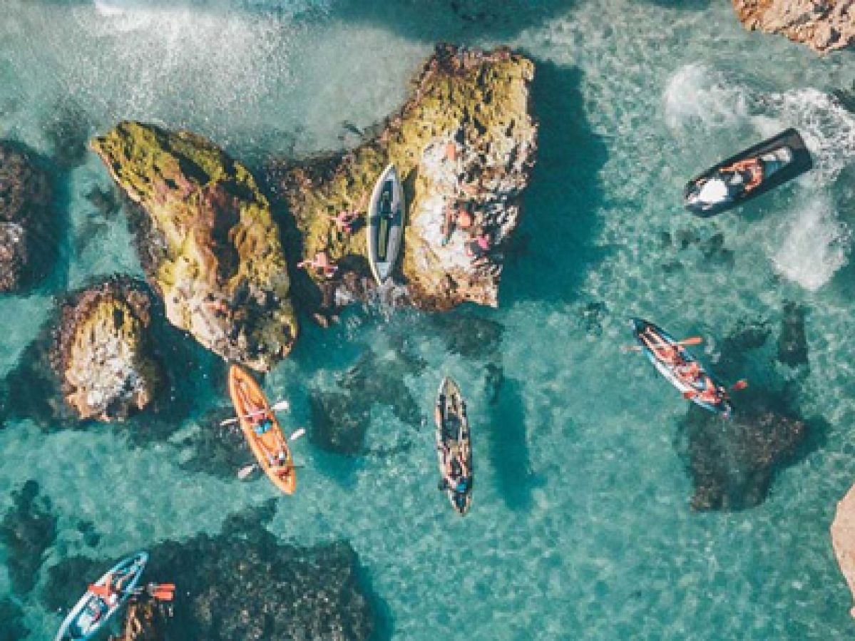 Aerial view of people kayaing in clear ocean waters near some rocks. 