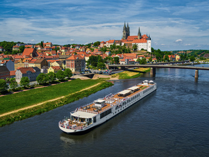 Long cruise ship going down a river alongside an old European town