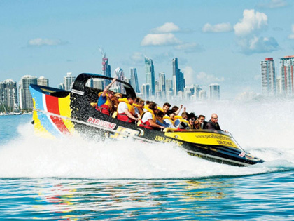 Paradise jet boat on the water infront of a city.