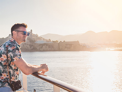 A traveller leaning on a cruise ship rail while observing the view.