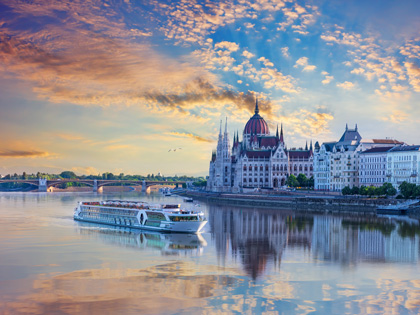 A cruise ship going past a castle in europe at sunset. 