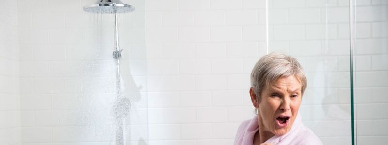 elderly woman standing away from leaking shower head