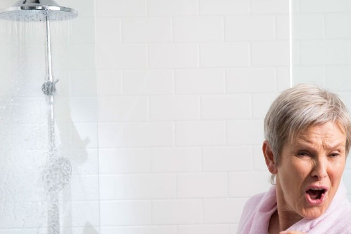 elderly woman standing away from leaking shower head
