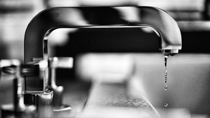 black and white image of faucet with water coming out