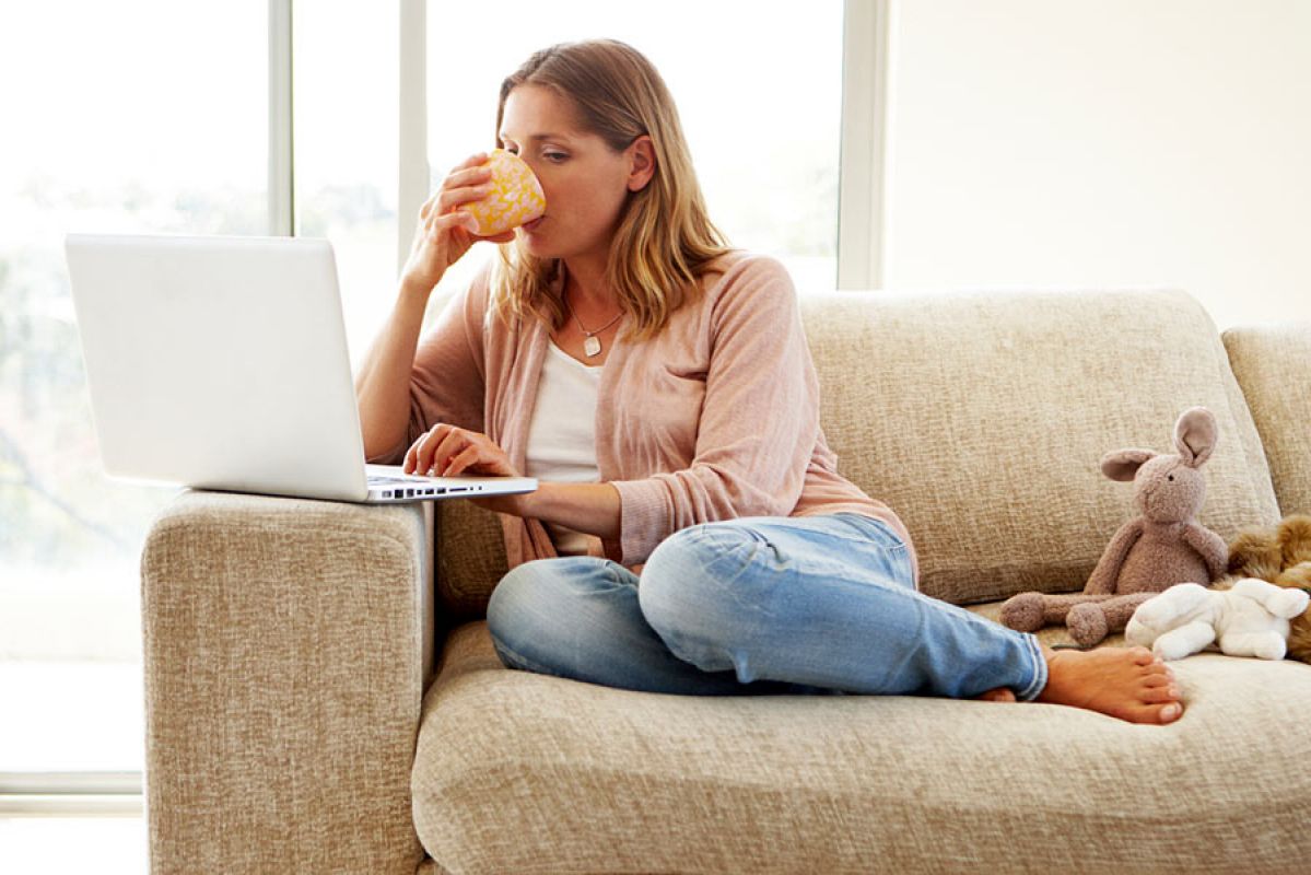 Woman working on laptop on couch while drinking coffee