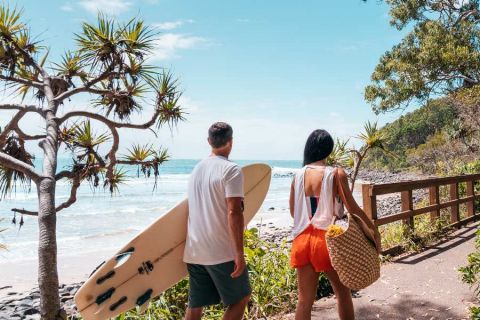 man and woman walking with a surfboard and bag through Noosa National Park