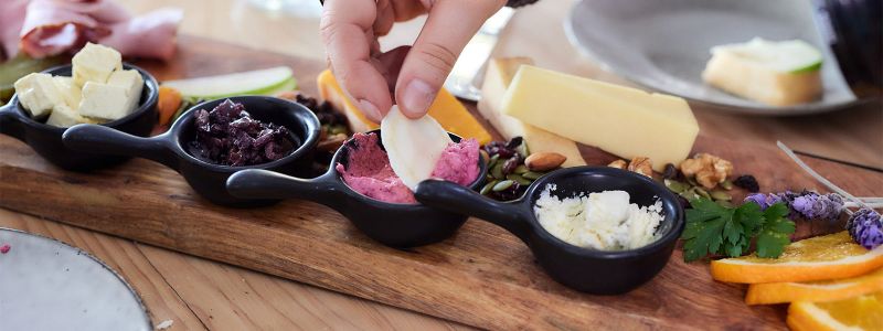 A person dipping a cracker into dip on a laden cheese platter at Bassine Specialty Cheeses