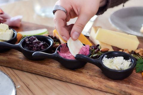 A person dipping a cracker into dip on a laden cheese platter at Bassine Specialty Cheeses