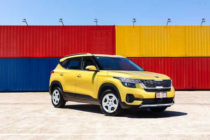 A yellow Kia Seltos park in front of coloured shipping containers 