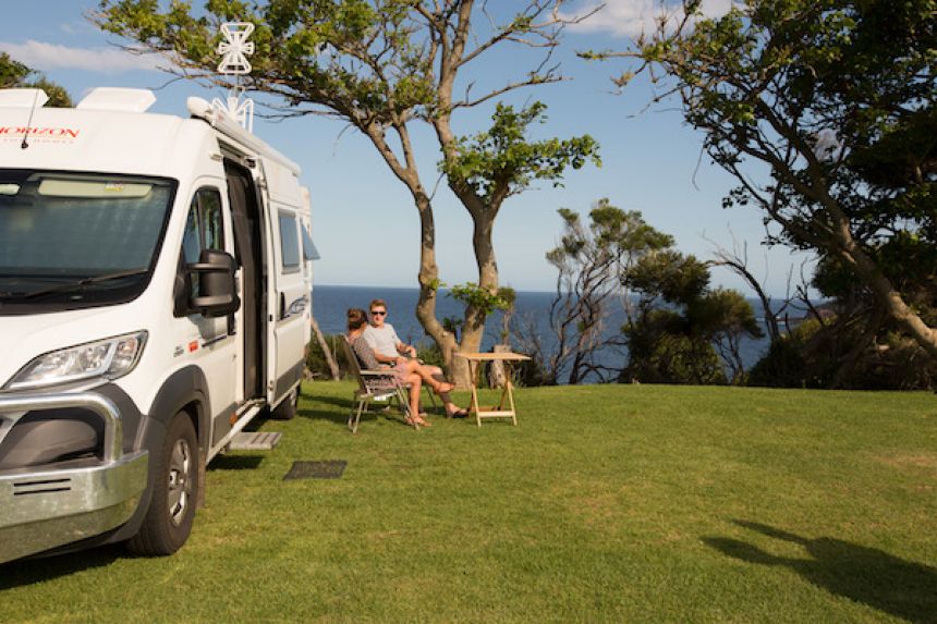 Couple sitting outside of camper van with the water visible in the background