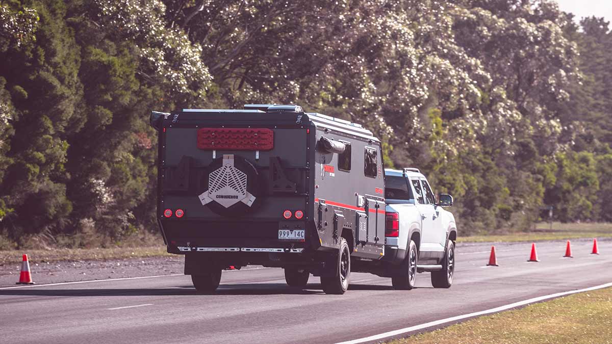 Rear view of white BYD Shark 6 Performance ute towing caravan on proving ground.