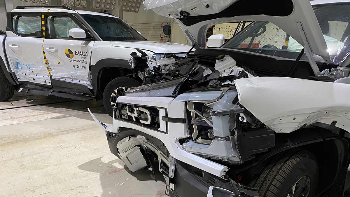 Two heavily damaged white BYD Shark 6 utes at crash test facility after ANCAP safety testing.