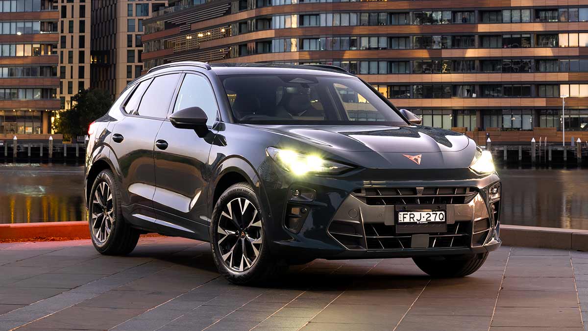 Dark Cupra Terramar SUV parked at riverside in city with apartment blocks behind