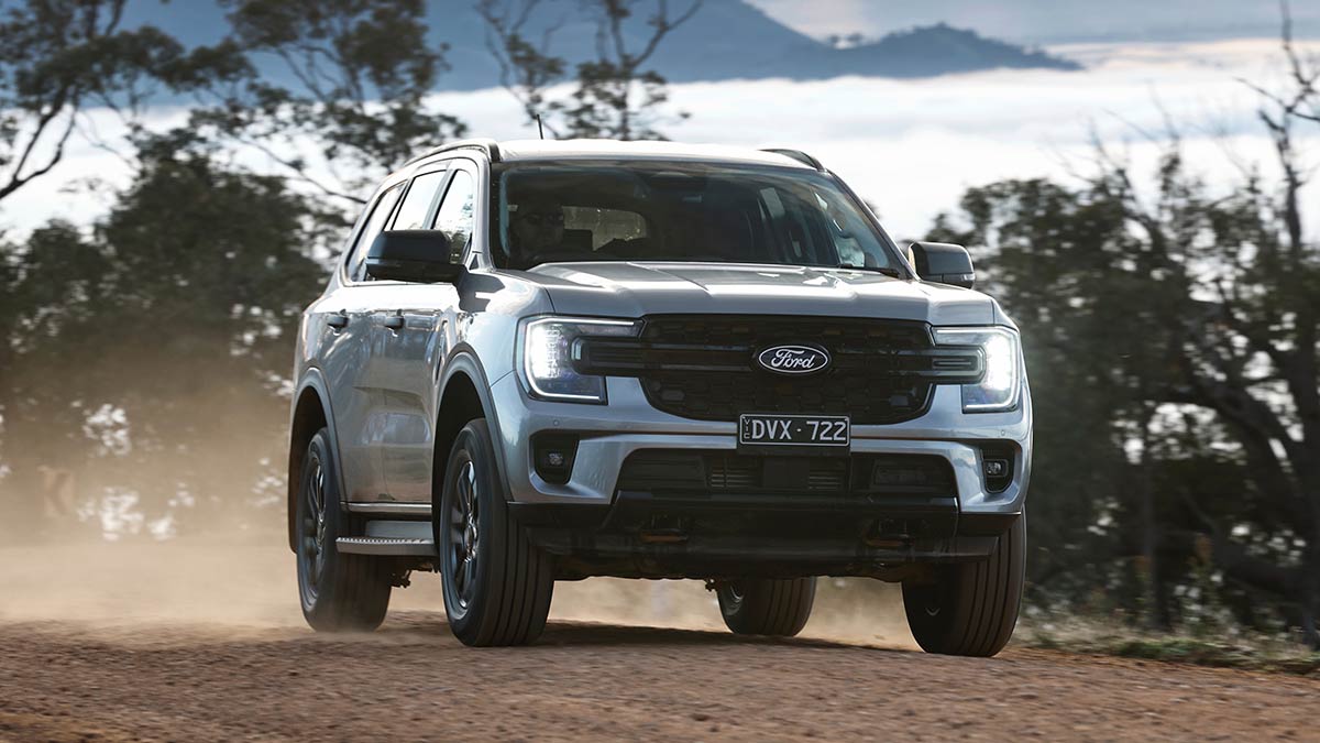 Silver metallic Ford Everest SUV on tree-lined gravel high country road above low-lying cloud.