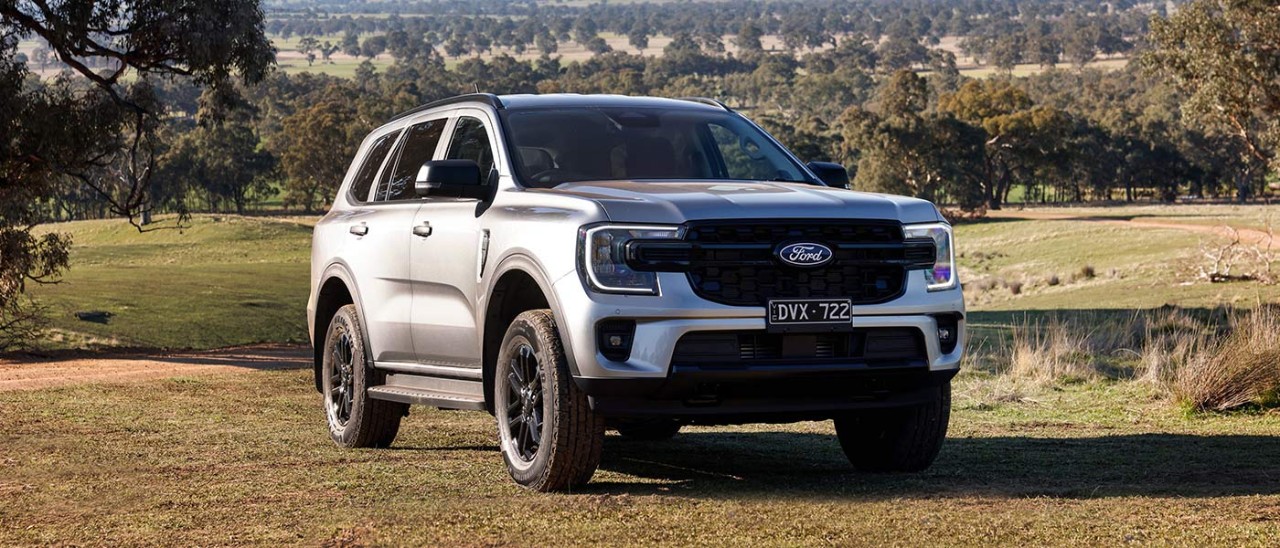 Silver metallic Ford Everest SUV on hillside of rural property with gravel road, paddocks and bush behind.