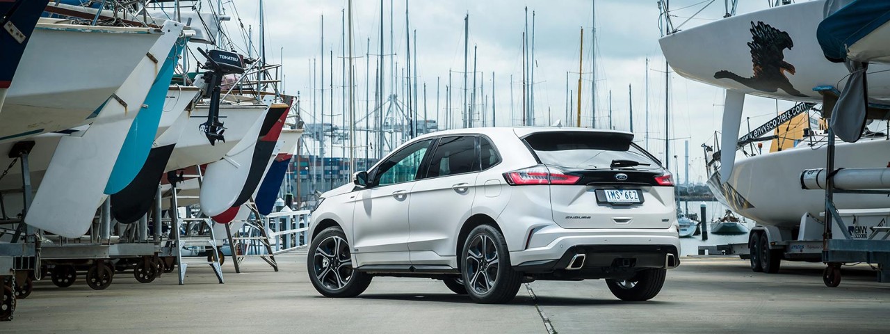 Rear side view of a white Ford Endura ST-Line 2019 car parked at a marina with parked boats on either side