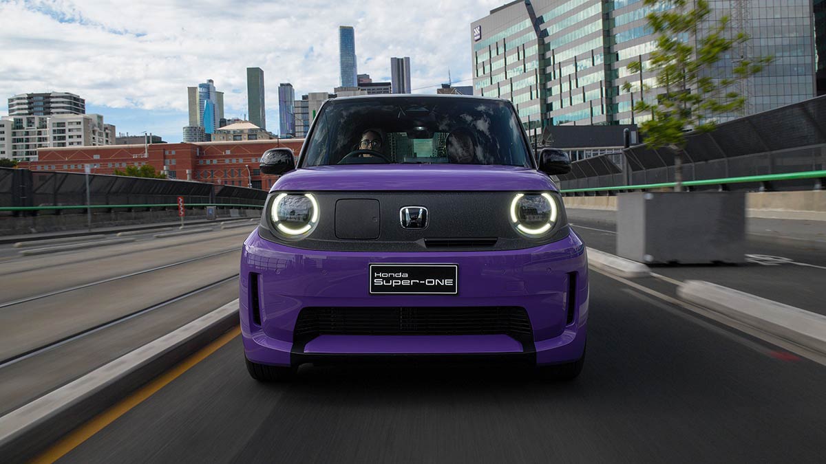Front-on shot of purple Honda Super-One driving in Melbourne CBD next to tram tracks with towers behind.
