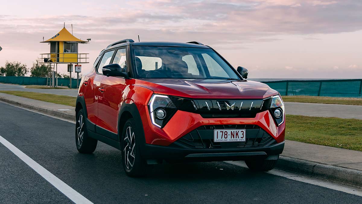 Red Mahindra XUV 3XO small SUV on beachside road with lifeguard tower behind