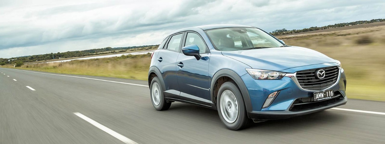 Front side view of a metallic steel blue Mazda CX-3 2017 car in motion on a road