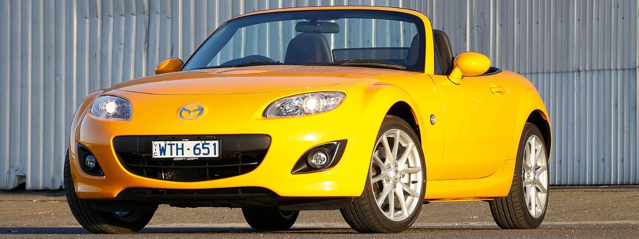 Front side view of a yellow Mazda MX-5 parked on a tarmac surface