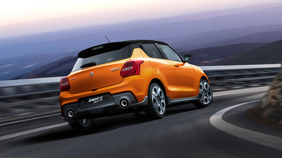 Rear side view of a bright orange Suzuki Swift Sport 2020 in motion