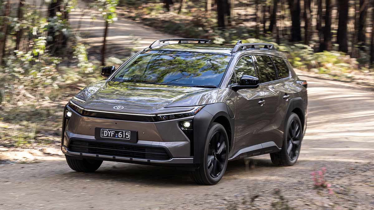 Bronze Toyota bZ4X Touring SUV rounding corner on gravel road in bush setting.
