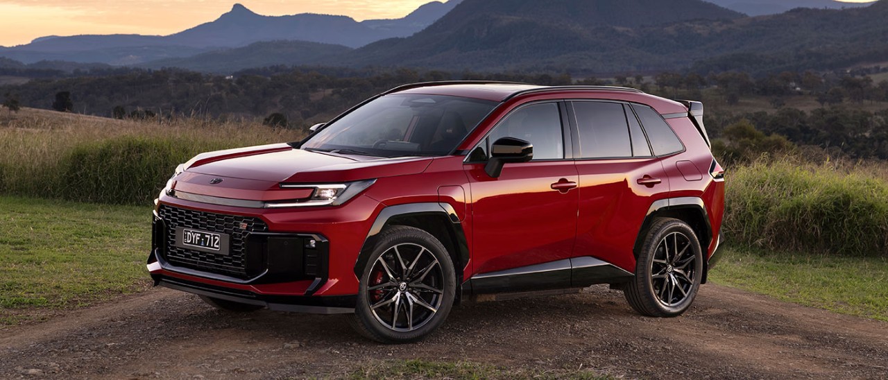 Red Toyota RAV4 GR Sport medium SUV parked across dirt track at base of mountain range at dusk