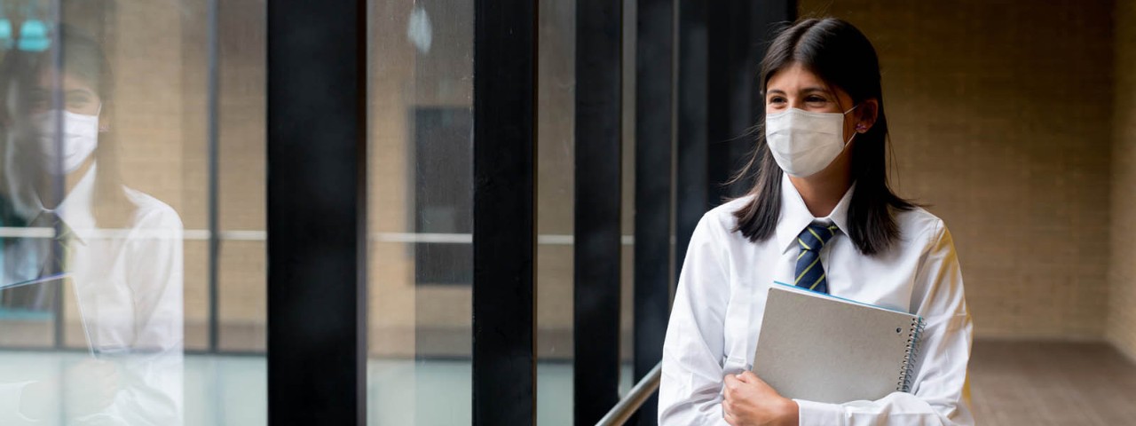 High school student wearing a mask holding notepad while looking out the window