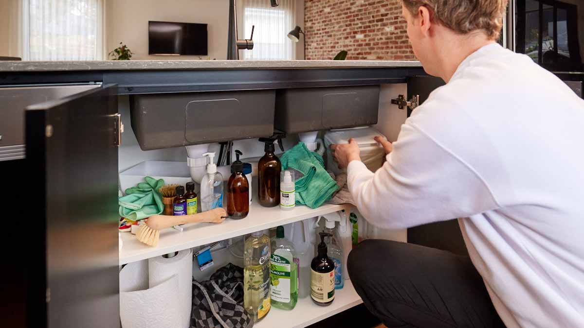 man tidying cleaning products under kitchen sink