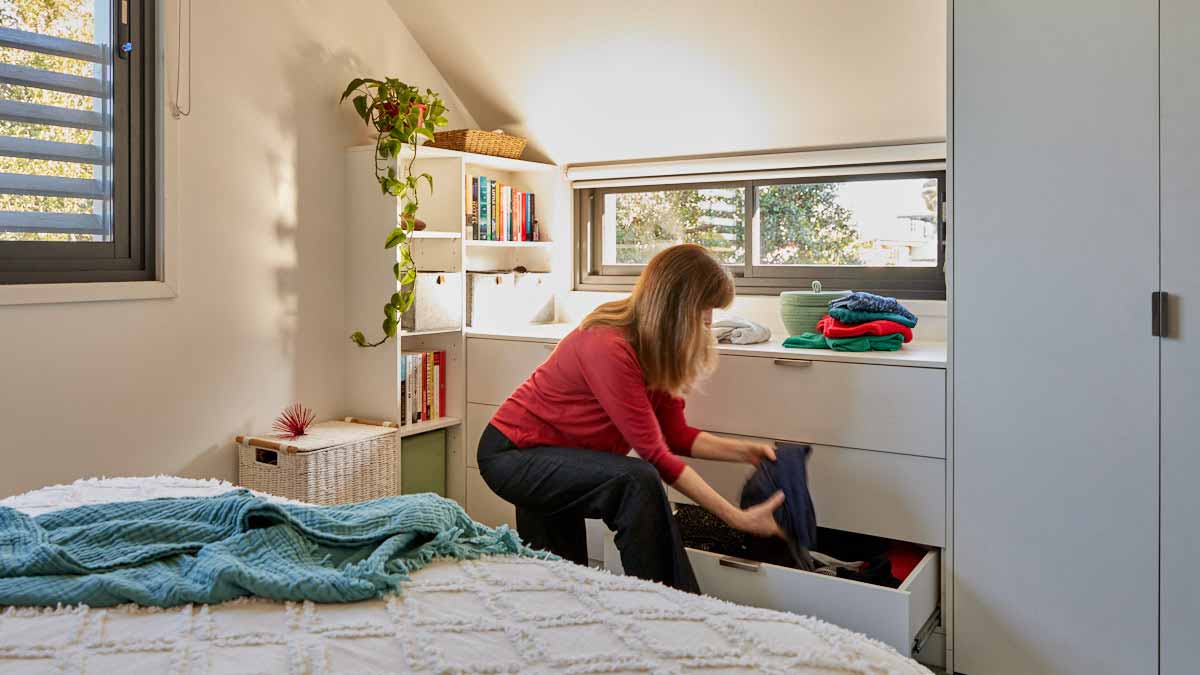woman putting away folded clothes into wardrobe drawers